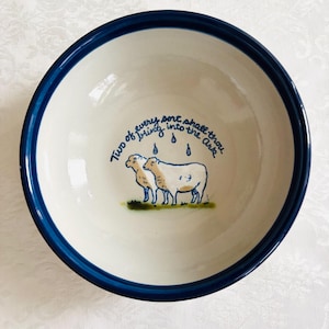 May include: A ceramic bowl with a cream-colored interior and a dark blue rim. The bowl features a hand-painted illustration of two sheep under raindrops, with the text "Two of every sort shall thou bring into the Ark."