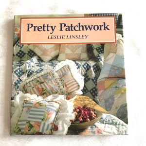 May include: A book titled "Pretty Patchwork" by Leslie Linsley, featuring a close-up of a patchwork quilt with pillows and dried flowers in a bowl.