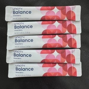 May include: Five white rectangular Unicity Balance Mixed Berry supplement sachets, each with a net weight of 7.25 g. The packaging features a geometric pattern of overlapping pink and red circles on the right side and dark blue text.