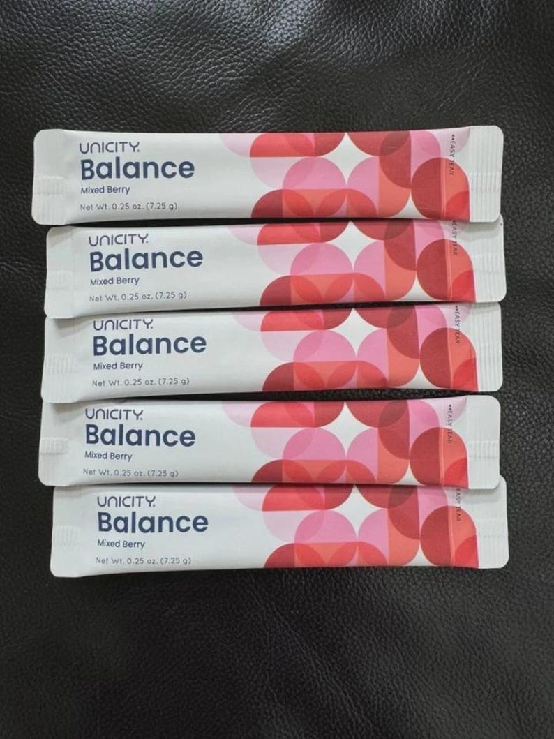 May include: Five white rectangular Unicity Balance Mixed Berry supplement sachets, each with a net weight of 7.25 g. The packaging features a geometric pattern of overlapping pink and red circles on the right side and dark blue text.