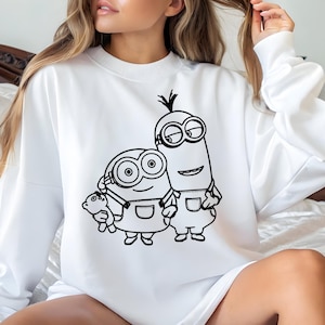 May include: White sweatshirt with a black graphic of two Minions. One Minion holds a teddy bear. The Minions are wearing dungarees and goggles. The sweatshirt has a crew neck.