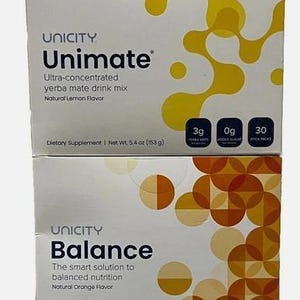 May include: Two rectangular boxes of Unicity dietary supplements stacked vertically. The top box is Unimate yerba mate drink mix in natural lemon flavour, net weight 153 g. The bottom box is Balance drink mix in natural orange flavour, net weight 217.5 g.