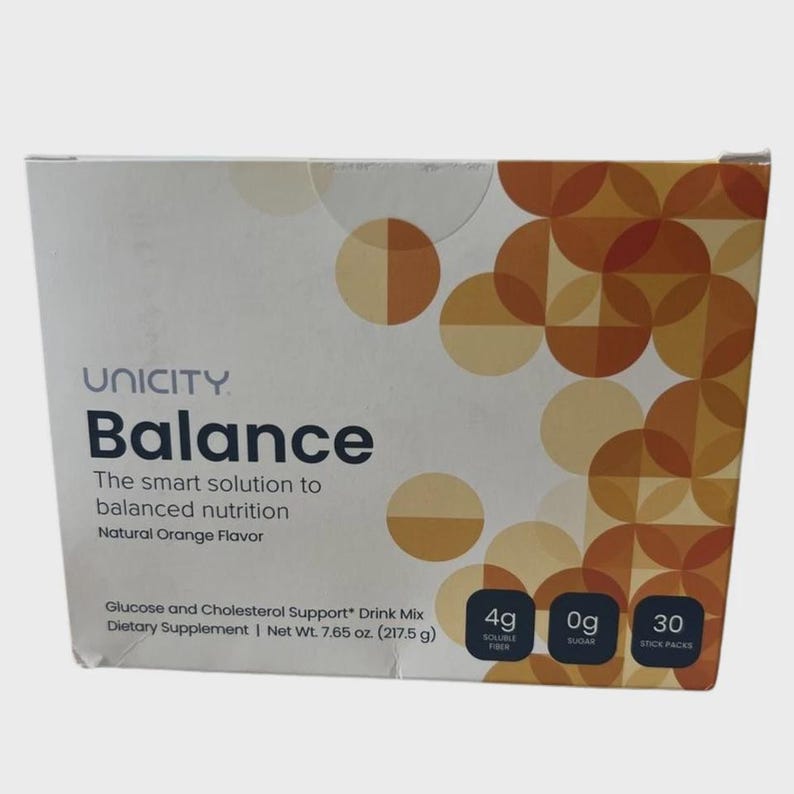 May include: A rectangular box of Unicity Balance dietary supplement drink mix with natural orange flavour. The white packaging features a geometric pattern of overlapping orange and tan circles, with text indicating 4g soluble fibre, 0g sugar, and 30 stick packs.