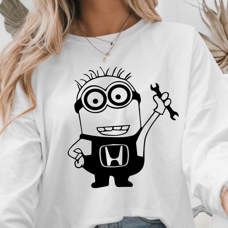 May include: White long-sleeved sweatshirt with a black and white cartoon minion holding a wrench. The minion is wearing a black jumpsuit with the Honda logo. The design is a fun take on automotive themes.