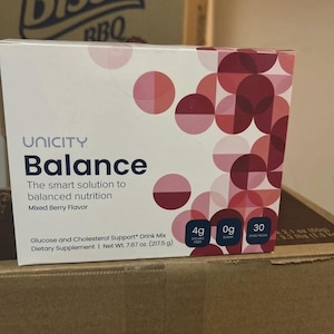 May include: A rectangular box of Unicity Balance dietary supplement drink mix in Mixed Berry flavour. The white packaging features a geometric pattern of overlapping pink and maroon circles, with text indicating 4g soluble fibre, 0g sugar, and 30 stick packs. Net weight is 217.5 g.