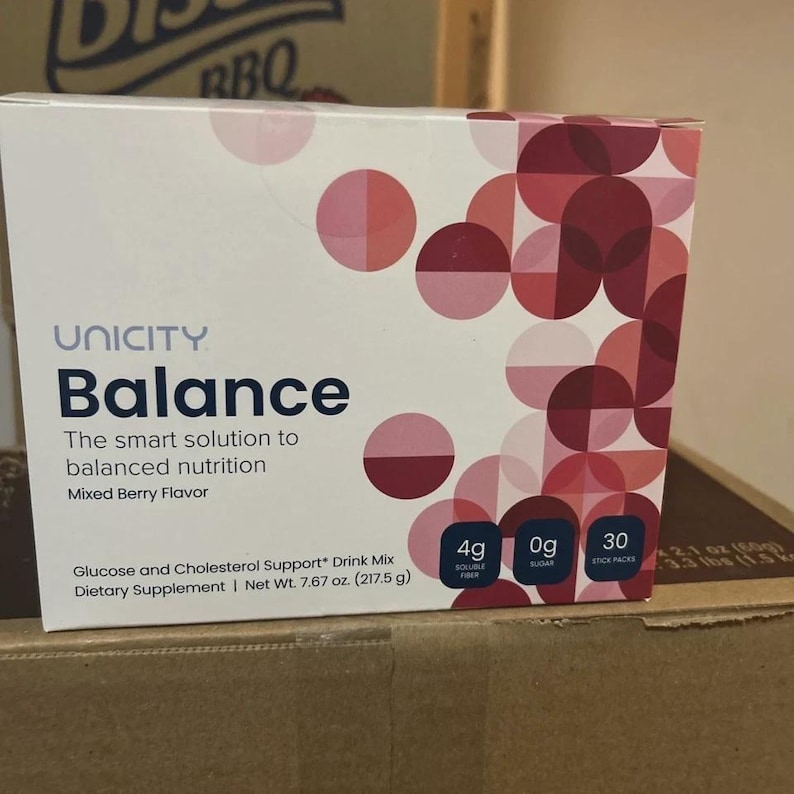 May include: A rectangular box of Unicity Balance dietary supplement drink mix in Mixed Berry flavour. The white packaging features a geometric pattern of overlapping pink and maroon circles, with text indicating 4g soluble fibre, 0g sugar, and 30 stick packs. Net weight is 217.5 g.