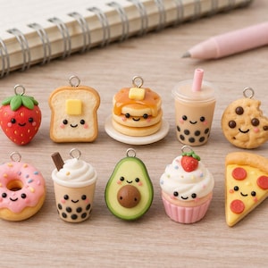 Puede incluir: Una colección de diez dijes en miniatura con temática de comida que incluye una fresa, pan tostado con mantequilla, panqueques, té boba, una galleta mordida, una dona glaseada rosa, una bebida boba con pajita, un aguacate, un cupcake y una porción de pizza.