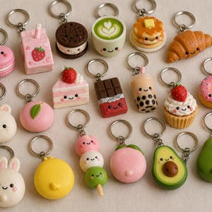 Könnte beinhalten: Eine Sammlung von Miniatur-Schlüsselanhängern in Form von Lebensmitteln und Tieren, darunter ein rosa Macaron, ein Erdbeermilchkarton, ein Schokoladen-Sandwich-Keks, ein Matcha-Latte, Pfannkuchen, ein Croissant, ein Kuchenstück, eine Schokoladentafel, ein Bubble Tea, ein Cupcake, ein Donut, Häschen, ein Pfirsich, Dango und eine Avocado.