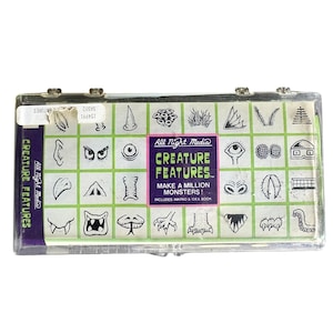 May include: A rectangular clear plastic case containing a set of rubber stamps titled All Night Media Creature Features. The label features a grid of black and white monster part illustrations, including eyes, teeth, and claws, with purple and green text.
