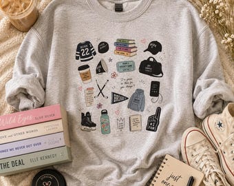 May include: A heather gray sweatshirt with various hockey-themed illustrations, including a jersey, books, and a hockey puck. The sweatshirt is paired with books, a notebook, and a pair of sneakers. A cup of iced coffee is also visible.