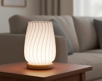 May include: A table lamp with a tapered, translucent white glass shade featuring vertical wavy lines. The lamp is supported by a circular, light-toned wooden base. The glass shade emits a soft, warm glow, illuminating the surrounding area.