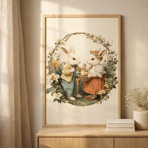 Pode incluir: Uma impressão emoldurada com dois coelhos antropomórficos em uma grinalda floral. Um coelho usa um casaco amarelo e calças azuis, o outro uma saia vermelha e uma coroa de flores, segurando uma cesta de ovos de Páscoa.