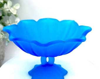 May include: A vibrant blue glass pedestal bowl with a scalloped rim. The bowl has a flower-like shape and sits on a star-shaped base. The bowl is made of opaque glass and is likely vintage.