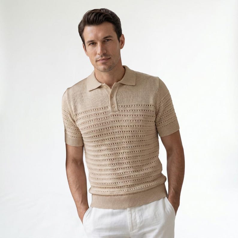 May include: A beige short-sleeved knit polo shirt featuring a textured open-stitch pattern across the chest and torso, a classic collar, a two-button placket, and ribbed cuffs and hem, paired with white trousers.
