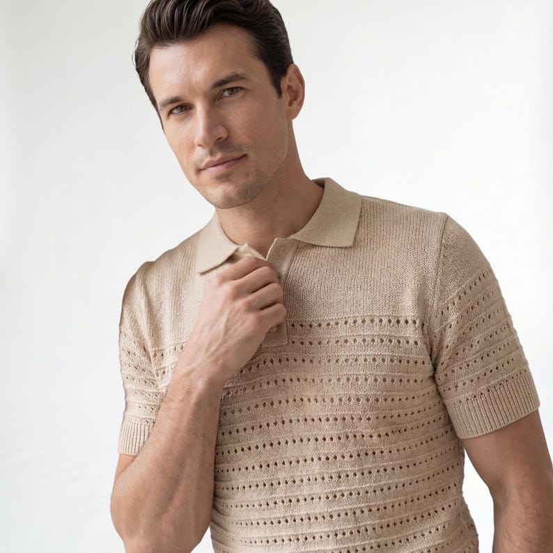 May include: A beige short-sleeved polo shirt featuring a textured knit fabric with horizontal rows of openwork detailing. The garment includes a classic collar and a partial button-front placket with matching beige buttons, finished with ribbed cuffs.
