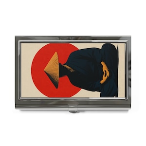 May include: A rectangular metal business card case featuring a graphic illustration of a person in a dark blue robe and a conical straw hat sitting in a meditative pose against a large, solid red circle on a cream-colored background.