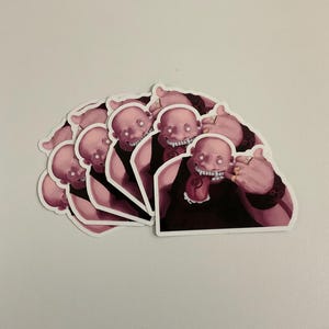 May include: A collection of stickers featuring a bald, pink-skinned character with a wide, toothy grin, wearing a black top and gold rings. The stickers are arranged in a fan shape, with a white border.