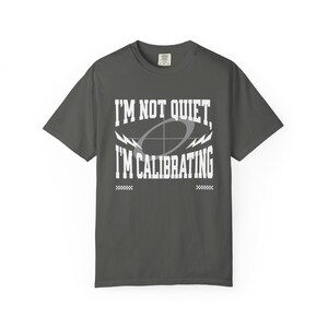 Puede incluir: Camiseta gris oscuro con el texto blanco "I'M NOT QUIET, I'M CALIBRATING". El diseño incluye un objetivo y rayos. La camiseta tiene cuello redondo y mangas cortas.