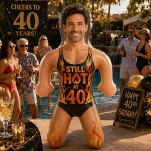 May include: An inflatable pool float shaped like a person with a printed face, wearing a black one-piece swimsuit featuring a flame pattern and the text "STILL HOT AT 40" in bold orange and yellow lettering, designed for a 40th birthday celebration.