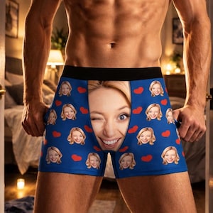 May include: Blue boxer shorts with a repeating pattern of smiling faces and red hearts. A large image of a smiling face is featured in the centre. The shorts have a black waistband.