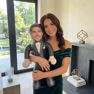 May include: A custom-shaped pillow featuring a photographic print of a person wearing a black tuxedo with a white shirt and a small white flower boutonniere. The pillow is shaped like a human figure with a head, torso, arms, and legs.