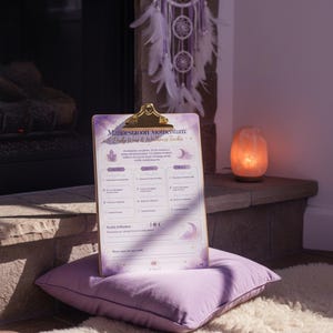 May include: A clipboard with a gold metal clip holding a printed sheet titled Manifestation Momentum: Daily Wins & Wellness Tracker. The paper features purple watercolor accents, moon phases, and sections for daily goals, reflections, and weekly intentions.