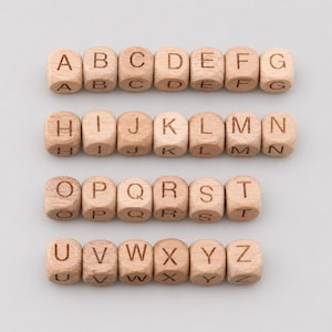 May include: Wooden alphabet blocks arranged in rows, each block displaying a letter from A to Z. The blocks are light brown with engraved letters, perfect for educational purposes or decorative use.