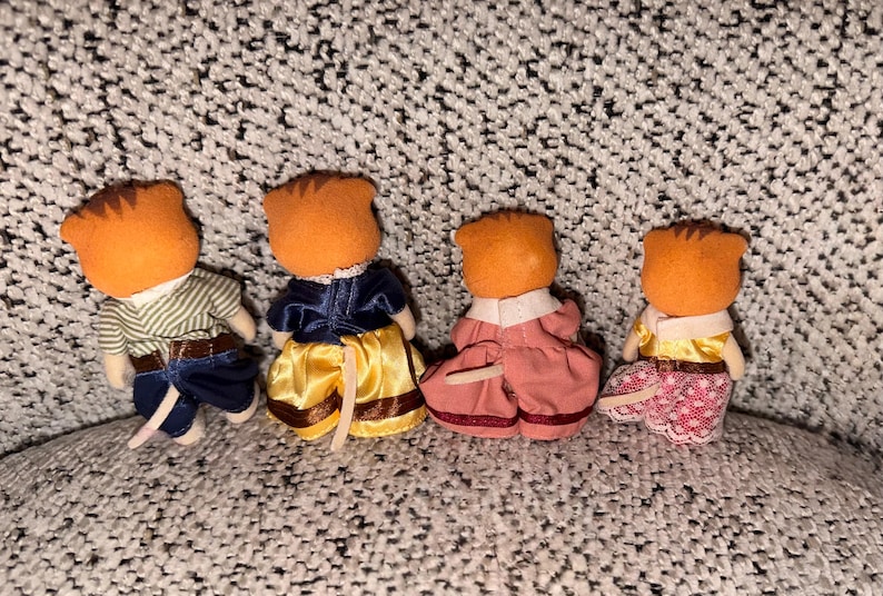 Puede incluir: Cuatro figuras de animales en miniatura con cabezas naranjas y varios atuendos. Uno viste una camisa a rayas y pantalones azules, otro una chaqueta azul y una falda amarilla, un tercero un vestido rosa y el &uacute;ltimo una blusa amarilla y una falda estampada.