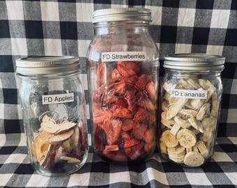May include: Three clear glass mason jars with silver metal lids, each containing freeze-dried fruit. The left jar is labeled FD Apples, the center jar is labeled FD Strawberries, and the right jar is labeled FD Bananas, filled with sliced fruit.