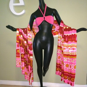 May include: A black mannequin wearing a pink halter top and a long, colorful patterned scarf. The scarf has a geometric design with pink, orange, and white colors.