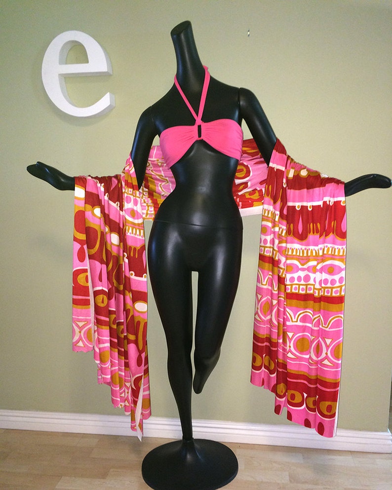 May include: A black mannequin wearing a pink halter top and a long, colorful patterned scarf. The scarf has a geometric design with pink, orange, and white colors.