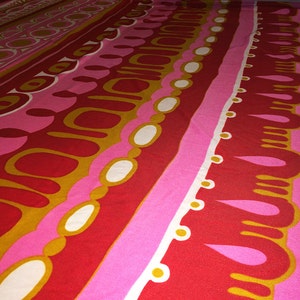 May include: Abstract patterned fabric with a repeating design of red, pink, white, and gold circles, ovals, and teardrop shapes.