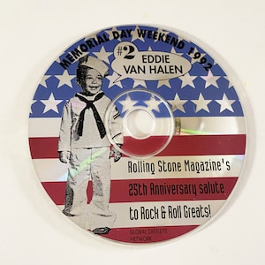 May include: A compact disc with a red, white, and blue American flag design. The disc features a cartoon image of Eddie Van Halen as a young boy in a sailor suit. The text on the disc reads "#2 Eddie Van Halen Memorial Day Weekend 1992 Rolling Stone Magazine's 25th Anniversary Salute to Rock & Roll Greats! Global Satellite Network."