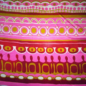 May include: A pink and red fabric with a repeating geometric pattern of circles, ovals, and arches. The pattern is in shades of pink, red, gold, and white.