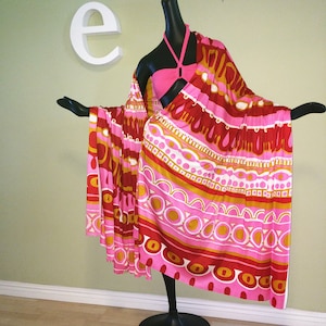 May include: A pink and red patterned sarong with geometric designs. The sarong is draped over a mannequin.