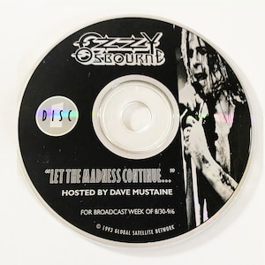 Pode incluir: Um CD preto com um rótulo de disco prateado que diz "DISC 1". O CD apresenta uma foto em preto e branco de Ozzy Osbourne cantando em um microfone. O texto no CD diz "Ozzy Osbourne", "Let the Madness Continue...", "Hosted by Dave Mustaine", "For Broadcast Week of 8/30-9/6", e "© 1993 Global Satellite Network".