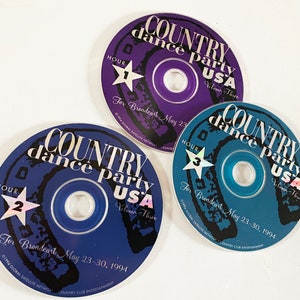 May include: Three compact discs with a blue, purple, and teal background. Each disc has a horseshoe design and the text "COUNTRY dance party USA Volume Three" with the hour number and text "For Broadcast May 23-30, 1994".
