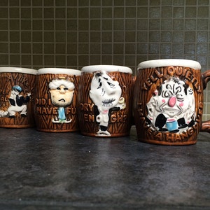 May include: Four brown ceramic mugs with cartoon faces and sayings. The mugs are shaped like tree trunks. The sayings on the mugs are "Yike, I'm a proper illegal thic", "Did I have fun", "Dry enough?", and "Yell quietly, I've a hang over".