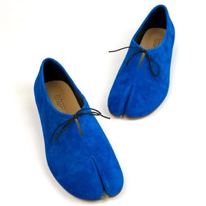 Può includere: Scarpe spaccate in camoscio blu brillante con lacci neri. Le scarpe hanno un design unico, con una sezione separata per l'alluce. Il marchio è visibile sulla soletta. Queste scarpe sono un'opzione di calzatura elegante.