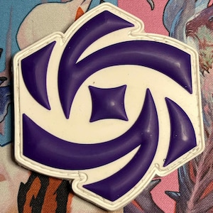 May include: A white and purple patch with a geometric design. The patch has a white border and a central design of swirling purple shapes and a small square. The patch is on a patterned background.