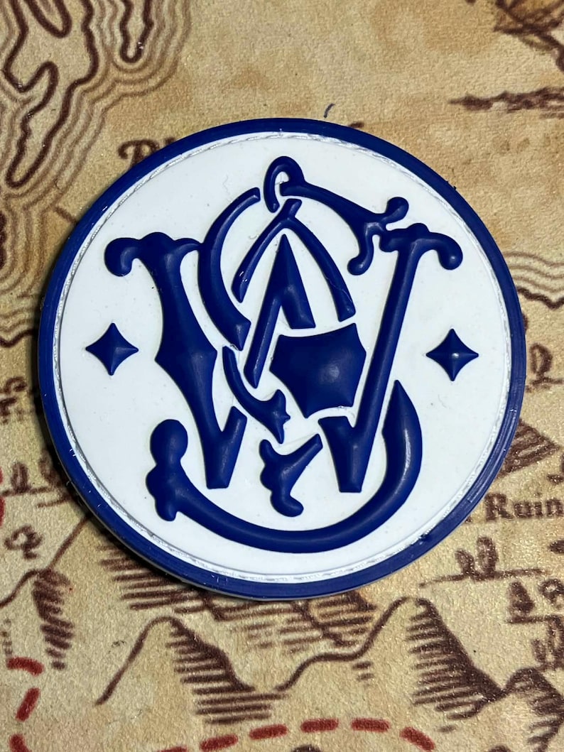 Peut inclure: Un embl&egrave;me rond blanc et bleu, avec les lettres stylis&eacute;es "S" et "W" entrelac&eacute;es avec un "A" central. L'embl&egrave;me a une bordure bleue et est pos&eacute; sur un fond de carte. Deux losanges bleus sont sur l'embl&egrave;me.