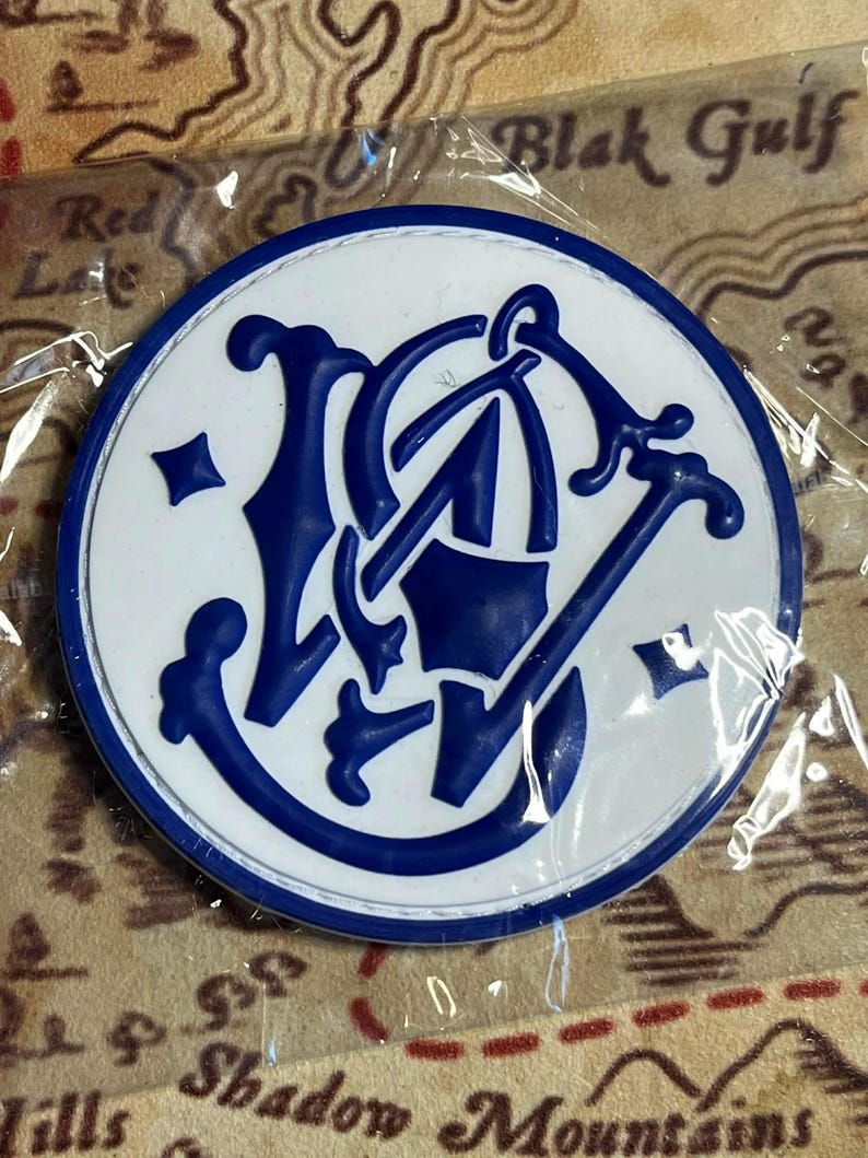 Peut inclure: Un embl&egrave;me rond, blanc et bleu, avec un motif stylis&eacute;. L'embl&egrave;me a une bordure bleue et un motif central bleu. L'arri&egrave;re-plan semble &ecirc;tre une carte.