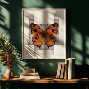 May include: A square framed wall art piece featuring a pixelated butterfly design in shades of orange, brown, and black. The butterfly is centered within a white background, and the frame is a simple, light-colored border.