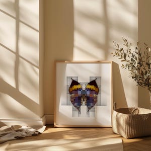 May include: A framed print with a pixelated butterfly design in yellow, purple, and blue hues. The artwork is presented in a light wooden frame, set against a white background with a geometric pattern. The room has a natural, sunlit atmosphere.