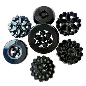 May include: A collection of six black buttons with various designs. The set includes two smooth circular buttons with cut-out centers, three intricate floral-patterned buttons with scalloped edges, and one button featuring a central square cutout.