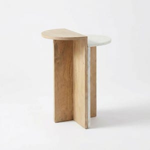 May include: A modern side table with a half-circle top. One half is light wood, the other is white. The base is made of light wood and a vertical strip of white material. The table is on a white background.