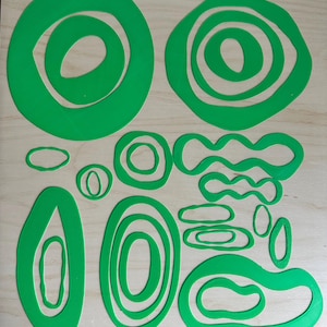 May include: A collection of bright green, abstract shapes in various sizes and designs. The shapes include circles, ovals, and wavy lines, all with a consistent, vibrant green color. The objects are arranged on a light-colored wooden surface.
