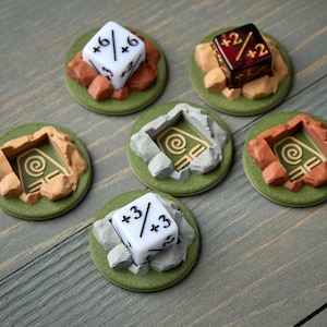 Puede incluir: Una colección de accesorios para juegos de mesa, que incluye dados y piezas de terreno. Los dados son blancos y rojos, mostrando varios números y modificadores. Las piezas de terreno son verdes, marrones y grises, diseñadas para parecer piedra y tierra.