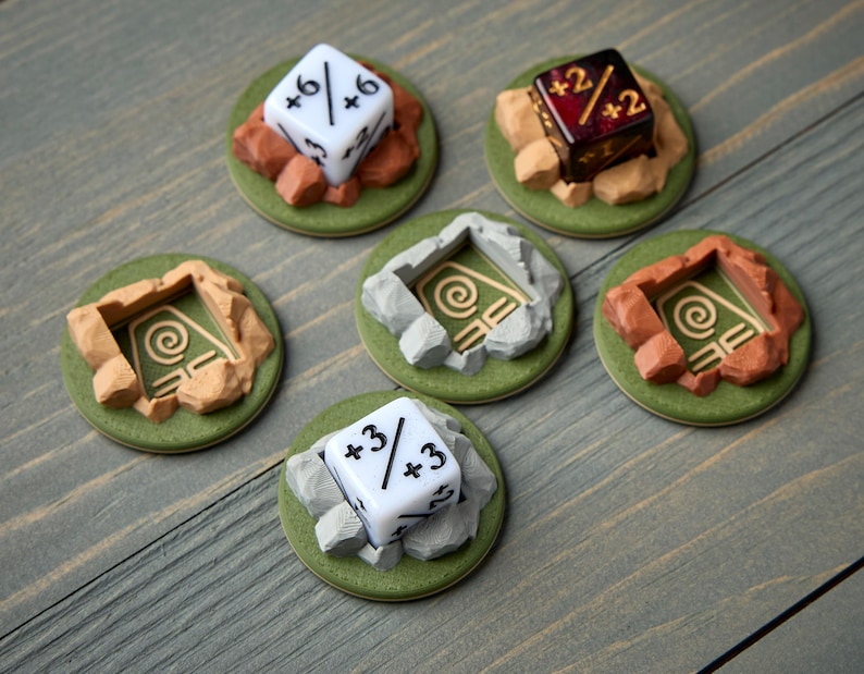 May include: A collection of tabletop gaming accessories, including dice and terrain pieces. The dice are white and red, displaying various numbers and modifiers. The terrain pieces are green, brown, and gray, designed to resemble stone and earth.