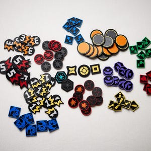 May include: A collection of colorful game tokens and markers in various shapes, including circles, squares, and irregular forms. The tokens feature a variety of colors such as black, orange, red, yellow, blue, green, and purple. Some tokens have numbers or symbols.